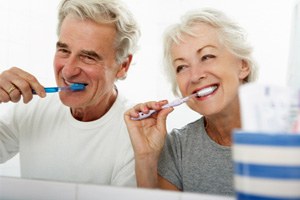 older couple brushing teeth in bathroom mirror 