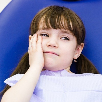 Little girl in dental chair holding jaw