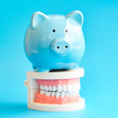 Piggy bank atop model teeth representing the cost of cosmetic dentistry in Springfield 