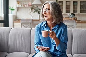 a woman drinking coffee and smiling with hybrid dentures