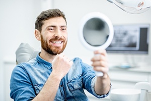 Man with dental implants in Springfield, MO smiling and looking at mirror