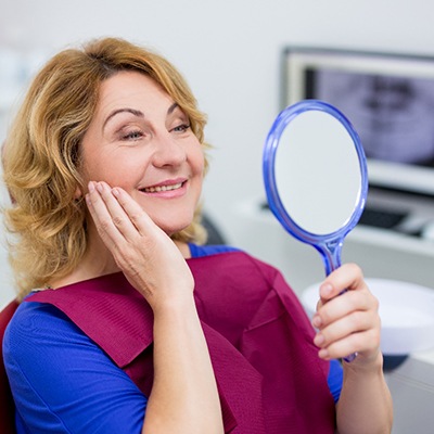 woman in dental chair admiring her smile 