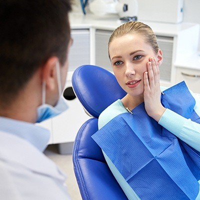 Woman in dental chair holding jaw