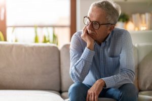 Man sitting on a couch with his chin in his hand thinking